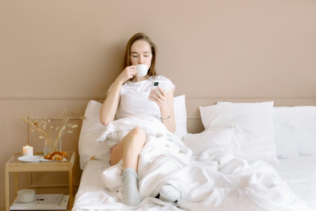 Uma mulher sentada na cama, tomando chá e lendo um livro, com expressão tranquila.